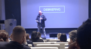Igor de chez repliks faisant un sketch lors d'un séminaire au grand rex avec le mot debriefing en arrière plan
